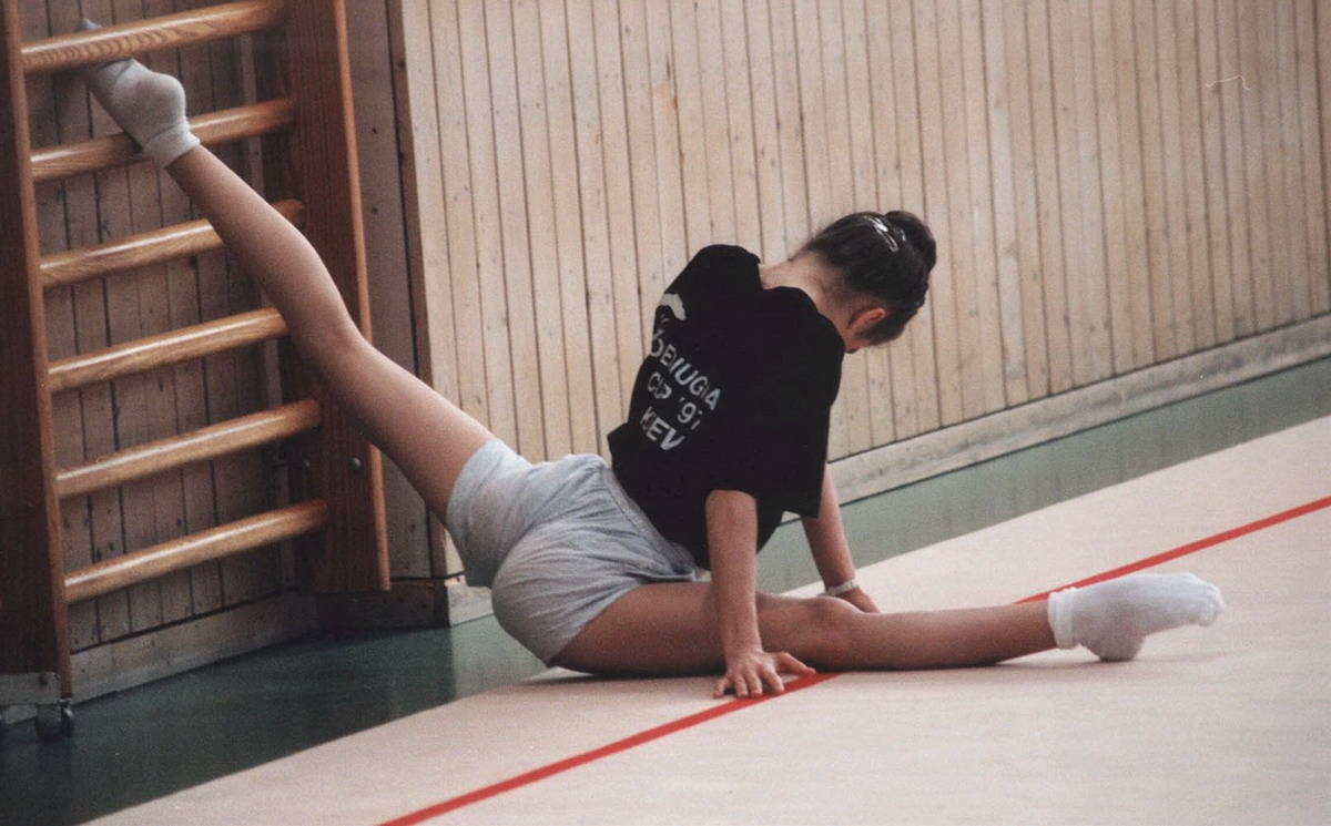 Худая девушка тренируется на гибкость голой лежа на мягком ковре
